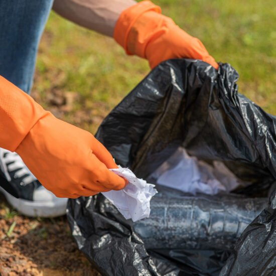 A man wearing orange gloves collecting garbage in a black bag. Selective focus.