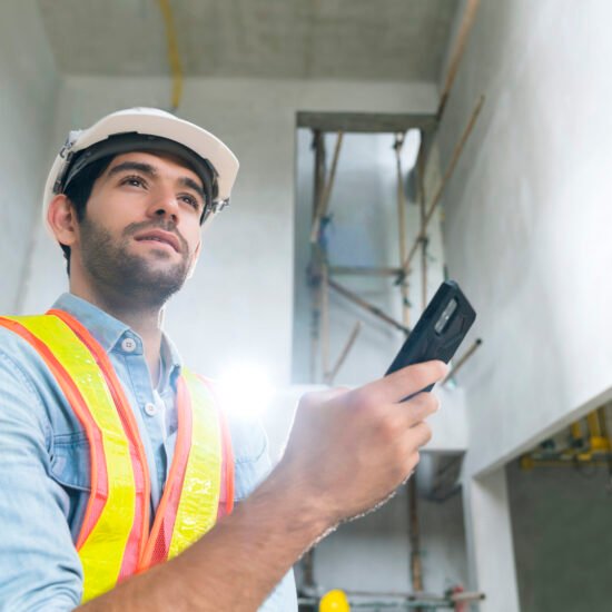 portrait of young caucasian male engineer wearing uniform and hard hat hand use smartphont communication in site construction background